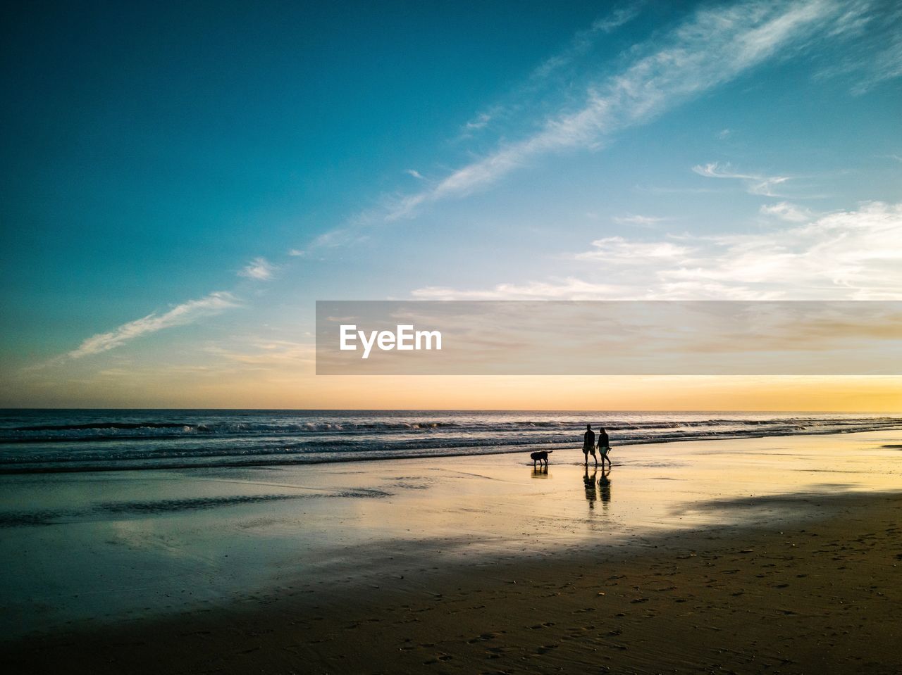 Scenic view of couple in the beach against sky during sunset