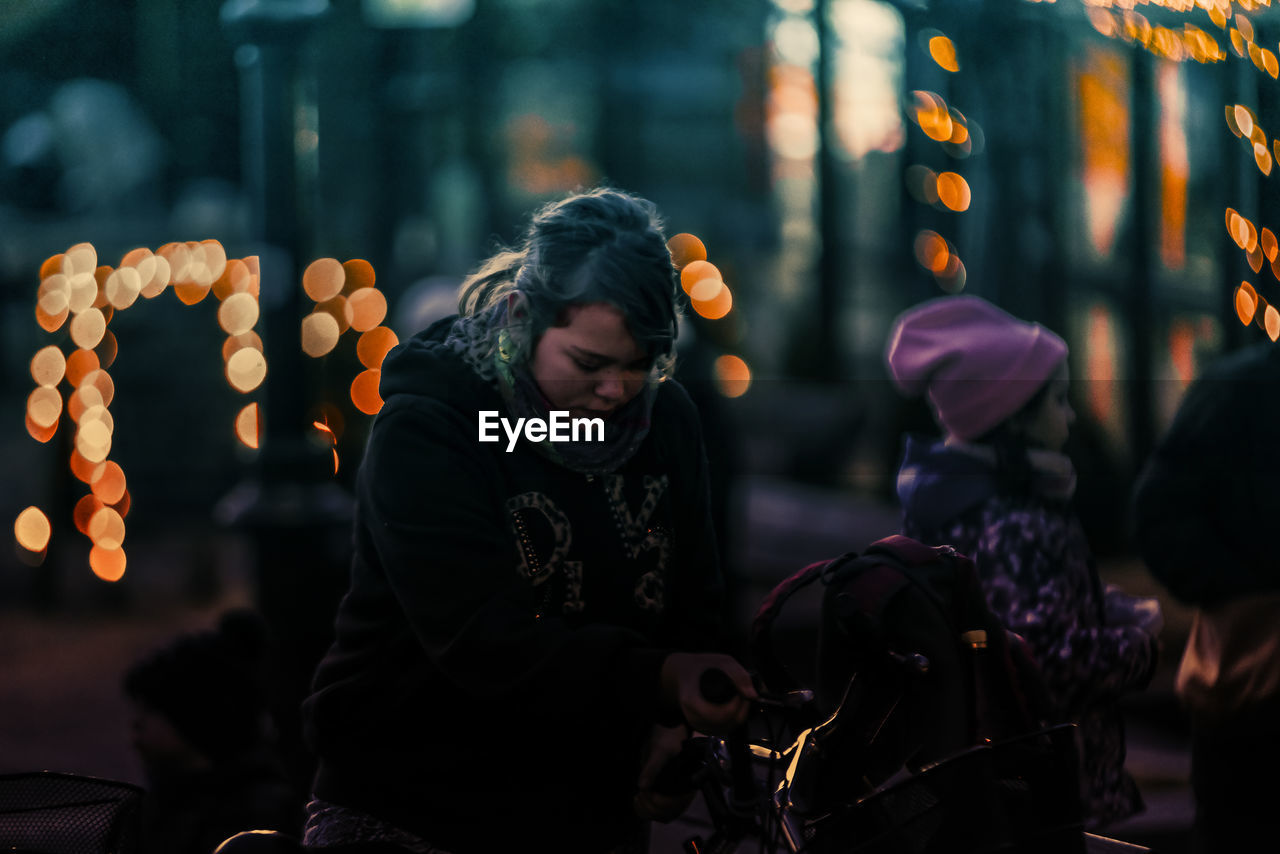 WOMAN LOOKING AT ILLUMINATED CITY IN NIGHT