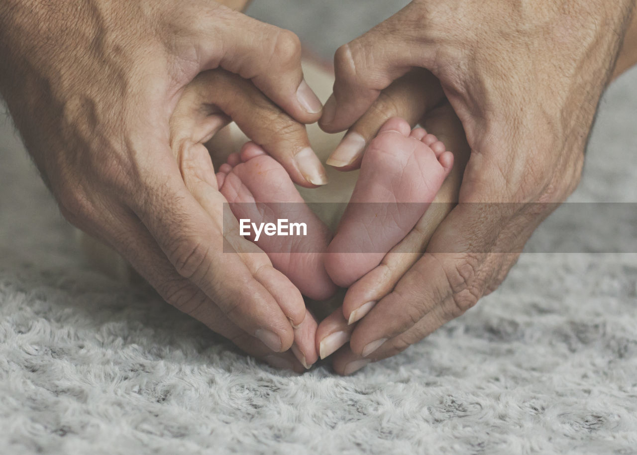 Cropped hands of parents forming heart shape around baby feet