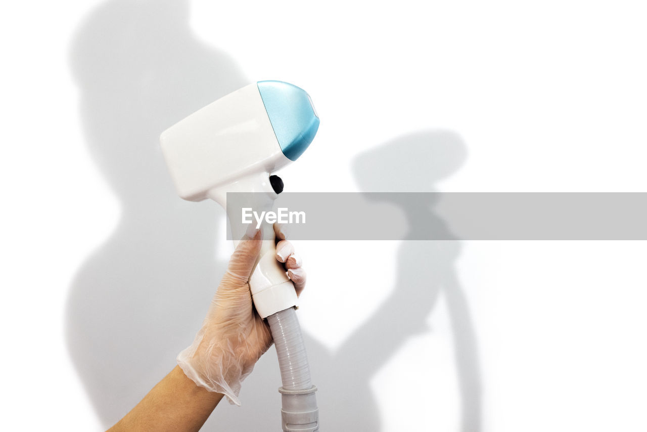 cropped hand of person holding dental equipment against white background