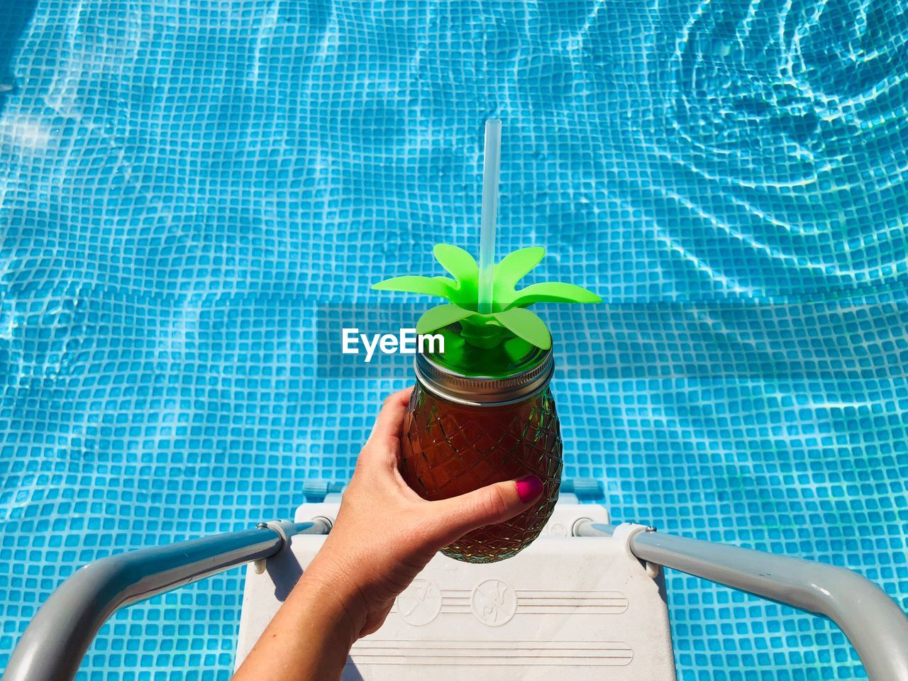 Cropped hand of woman holding drink over swimming pool