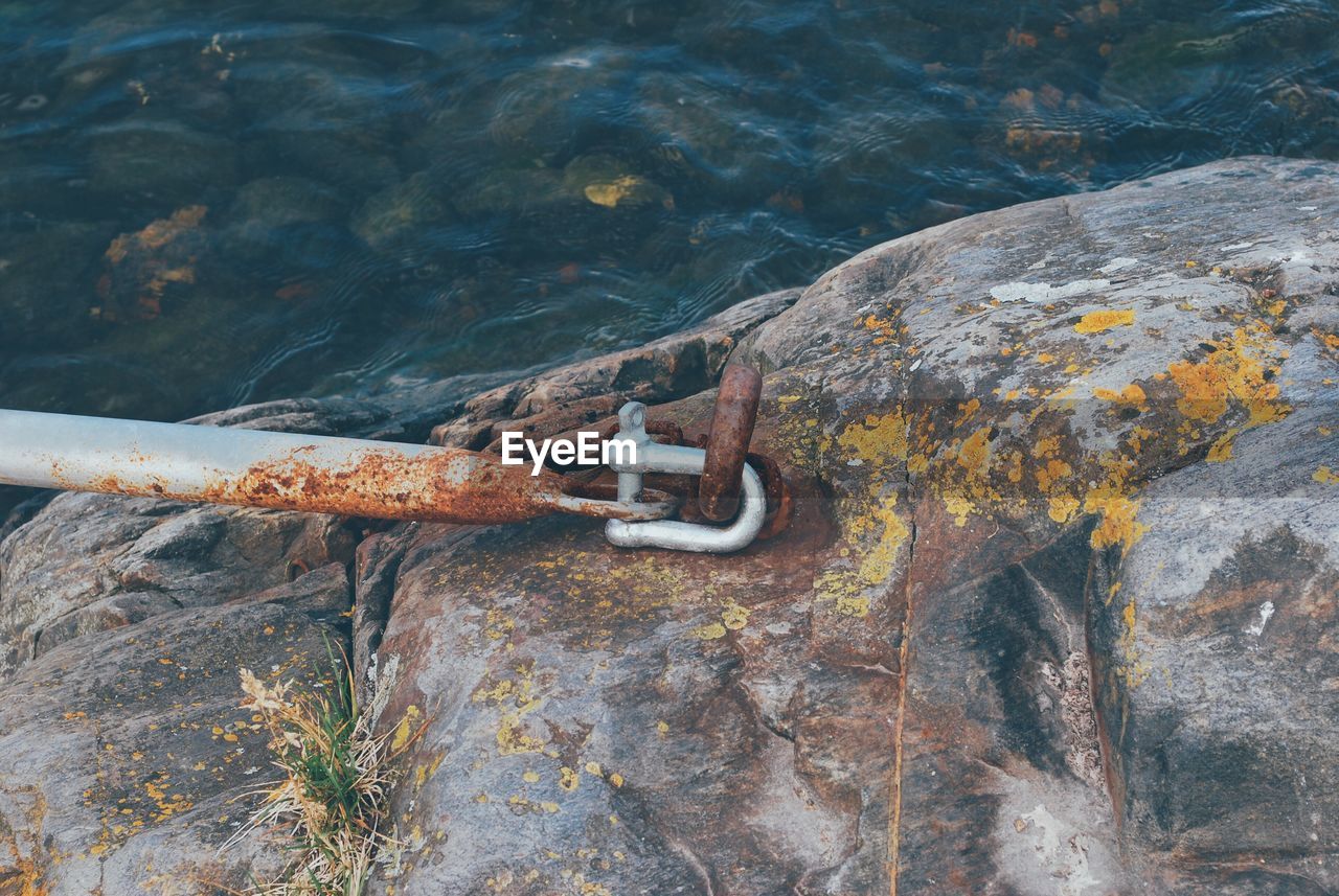 CLOSE-UP OF RUSTY CHAIN ON ROCK BY WATER