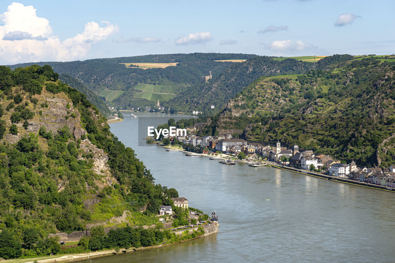 The river rhine in western germany flows between the hills covered with forest, visible buildings.