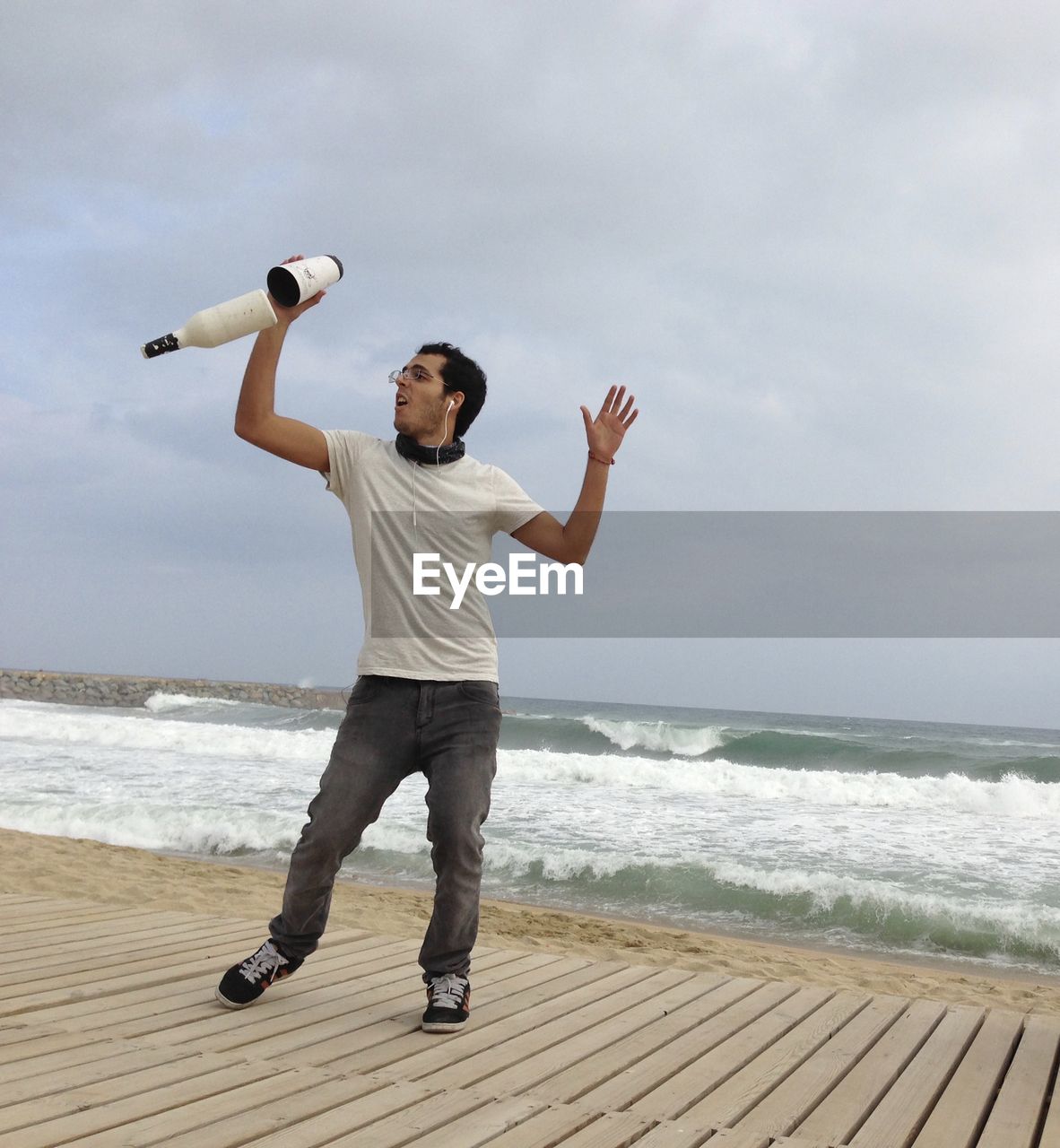 Full length of man juggling bottles on boardwalk at beach against sky