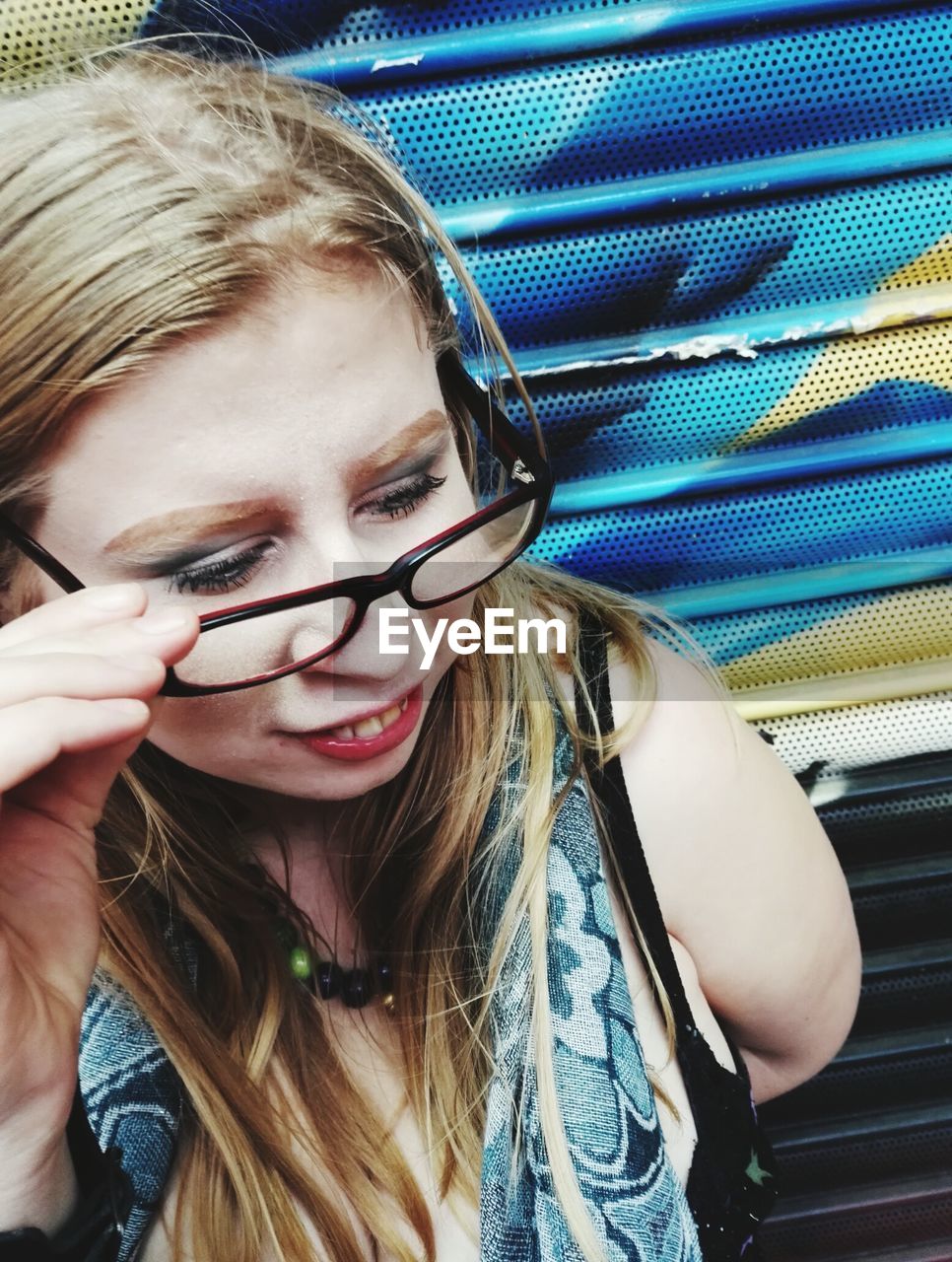 High angle view of woman holding eyeglasses while standing against closed shutter