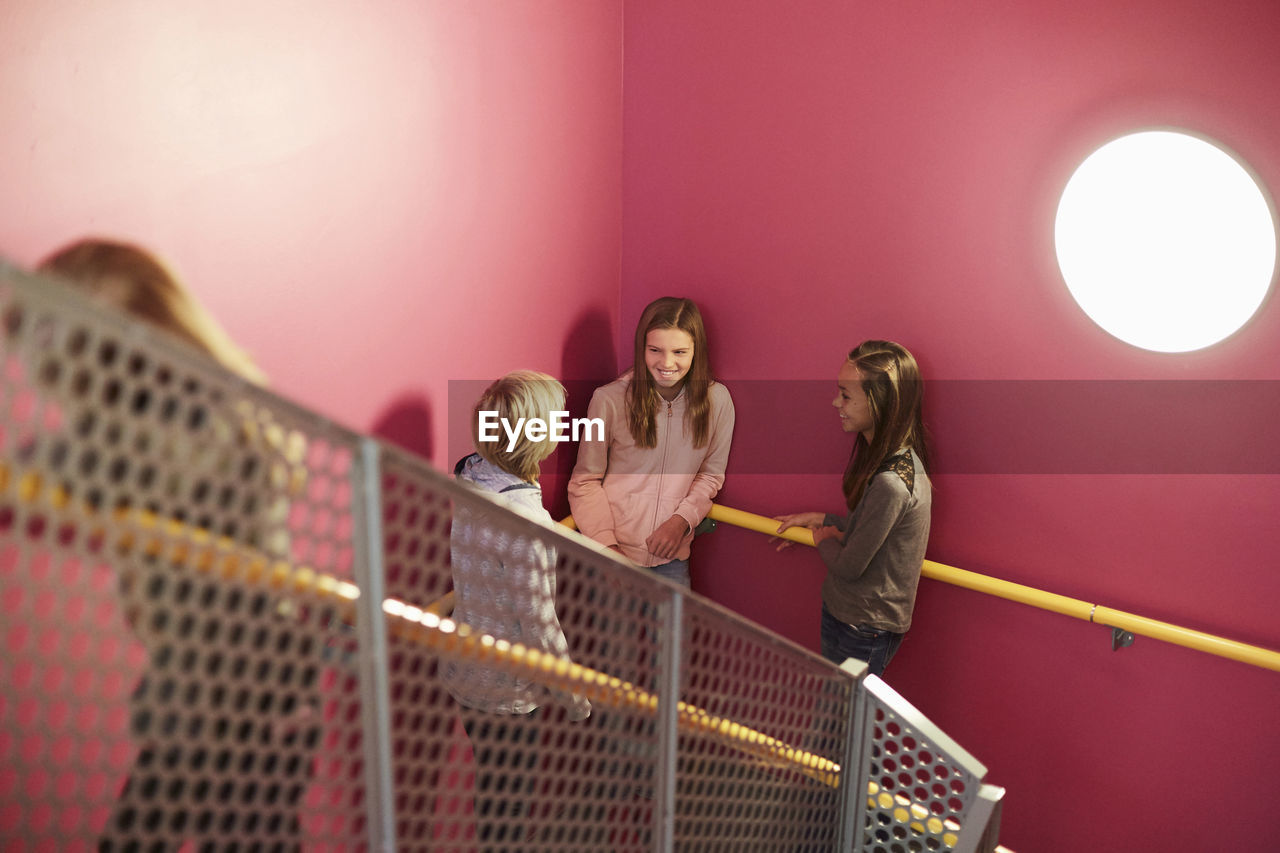 Smiling girl talking with friends against pink wall in middle school