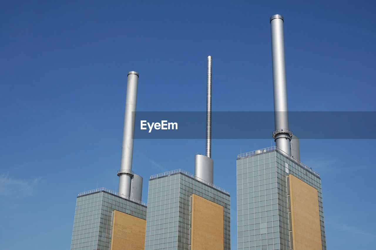 Low angle view of smoke stacks on factories against blue sky