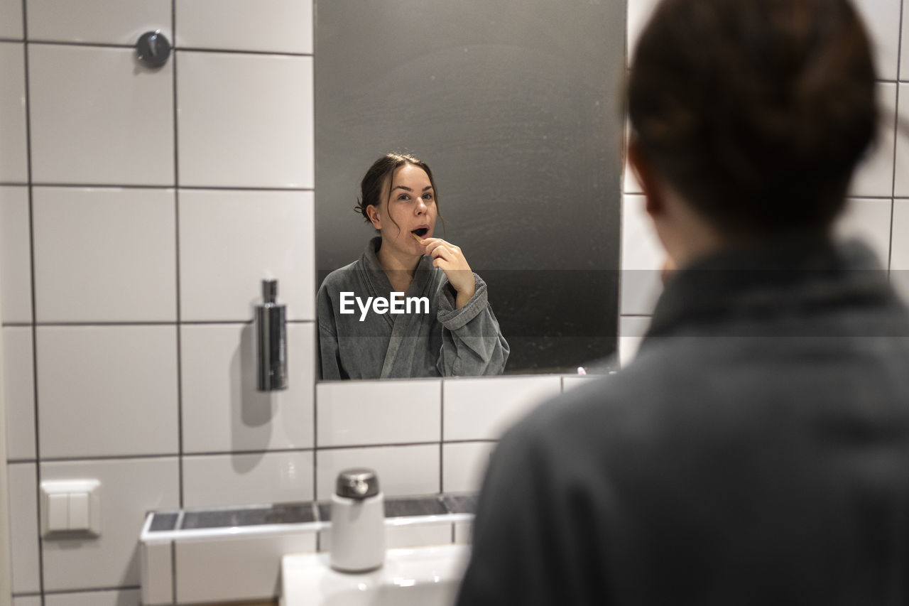 Mirror reflection of young woman brushing teeth in bathroom