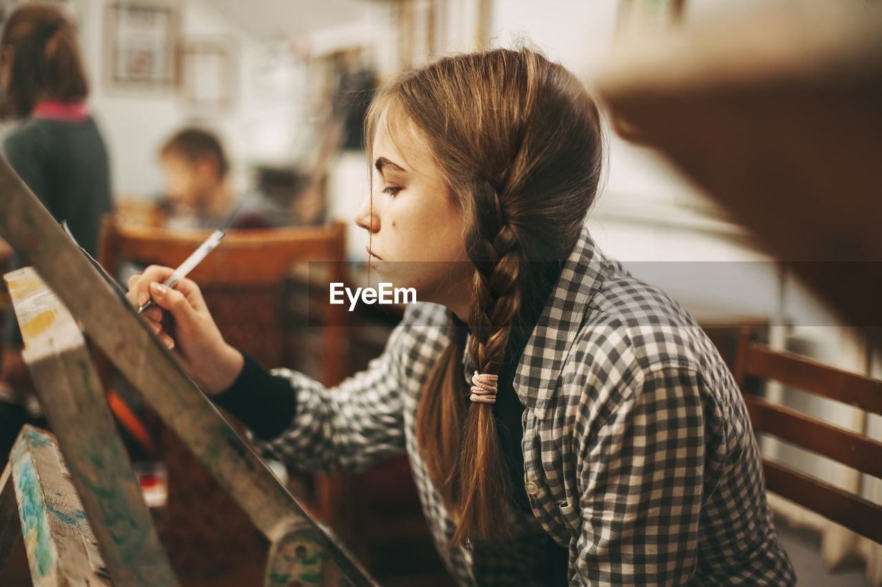 Beautiful teenage girl at art school painting on easel, art studio