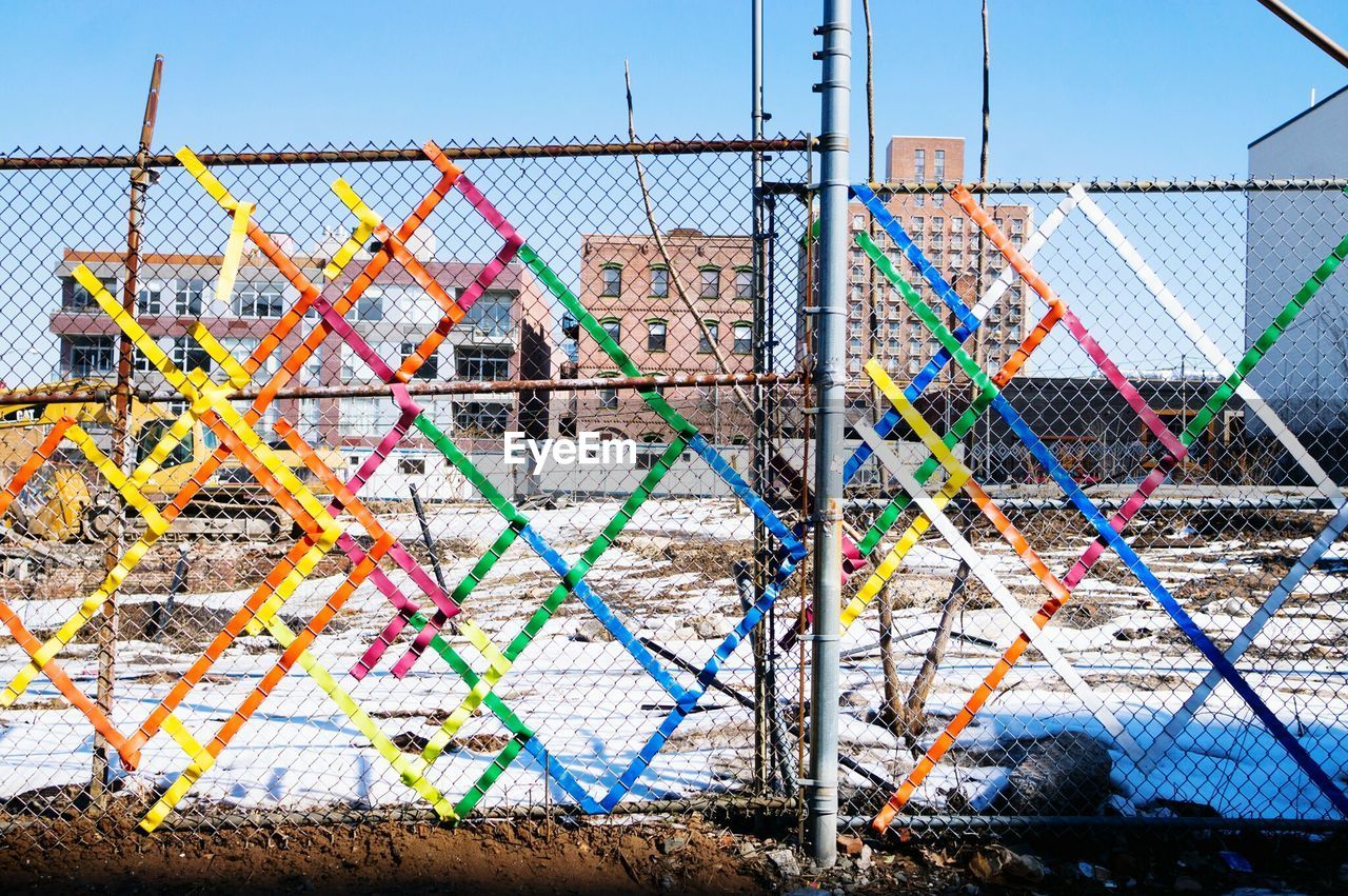 Multi colored pattern on chainlink fence against buildings