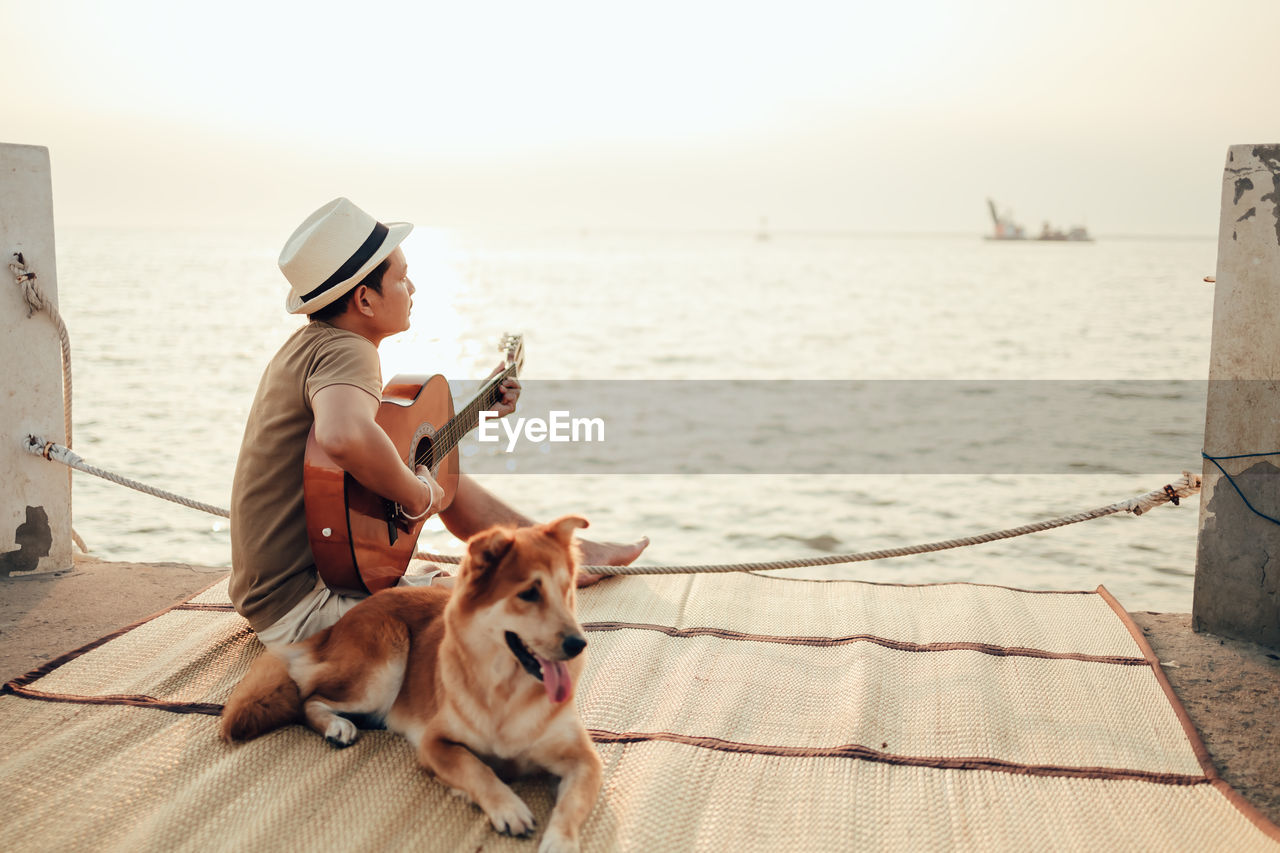 Man with dog sitting against the sky