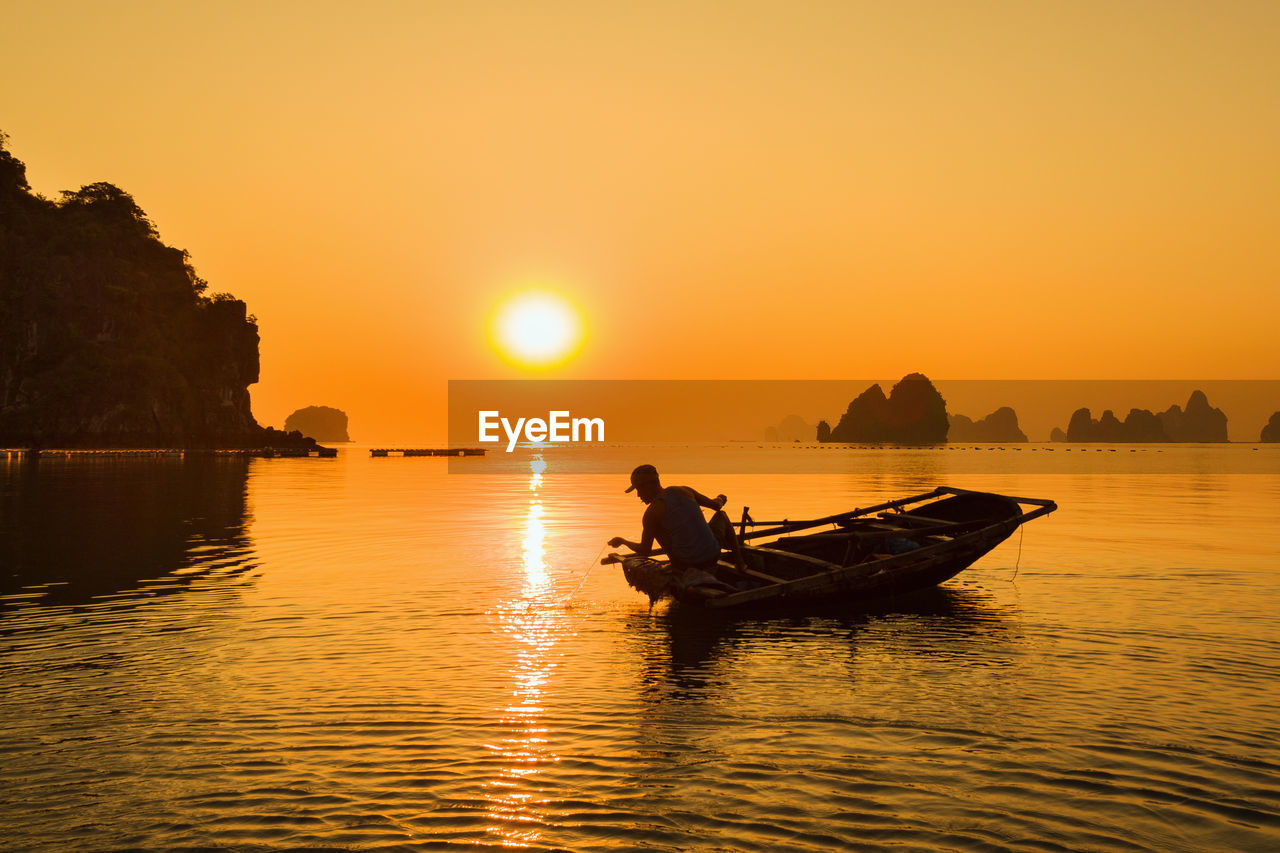 Silhouette man sitting on boat in sea against sky during sunset