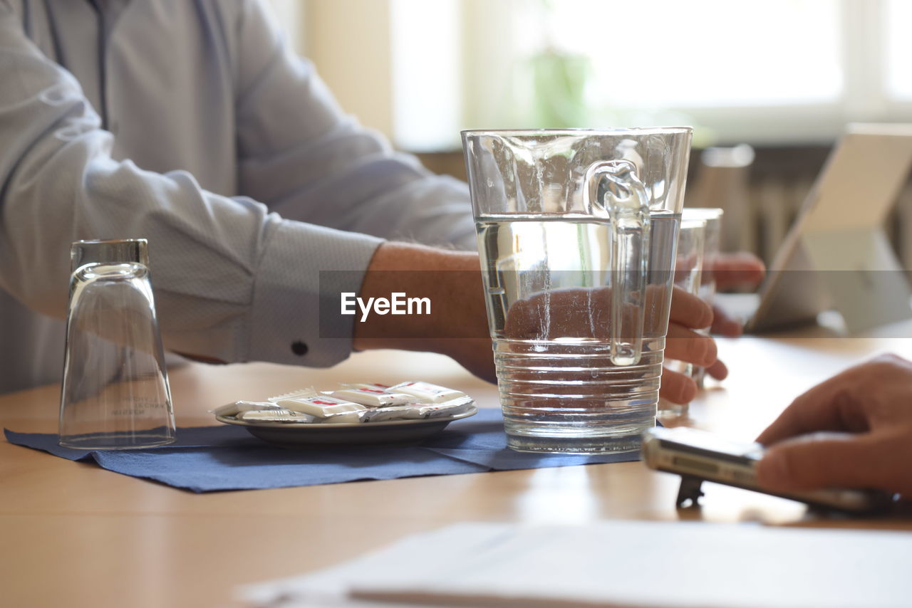 midsection of man using mobile phone at table