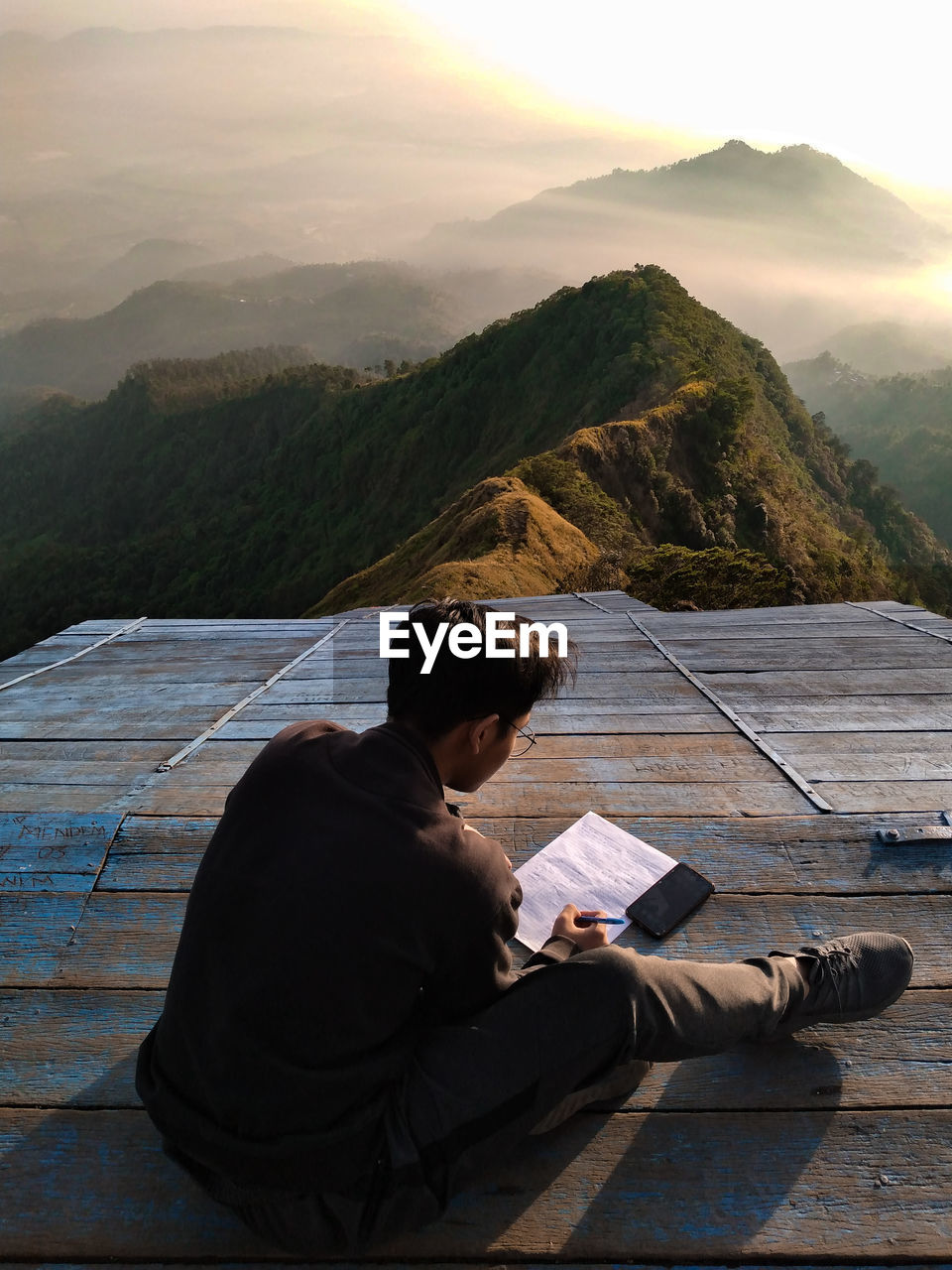 Man sitting on book by mountains against sky