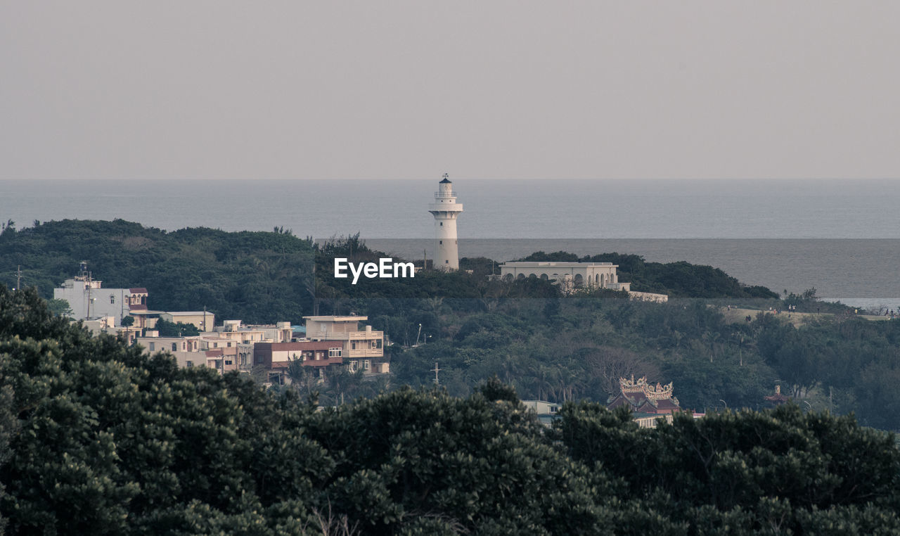 Lighthouse amidst buildings and sea against sky