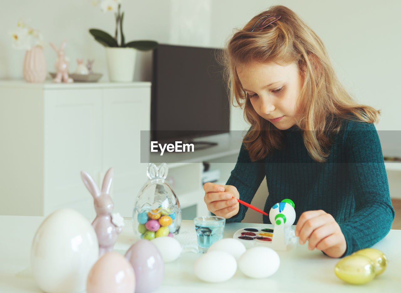 Cute girl painting easter egg while sitting at home