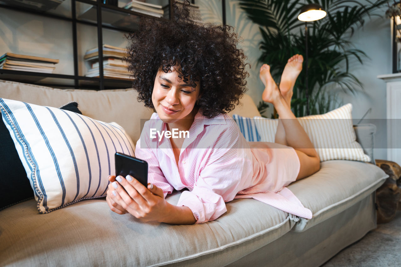 Young woman using mobile phone while lying on sofa at home