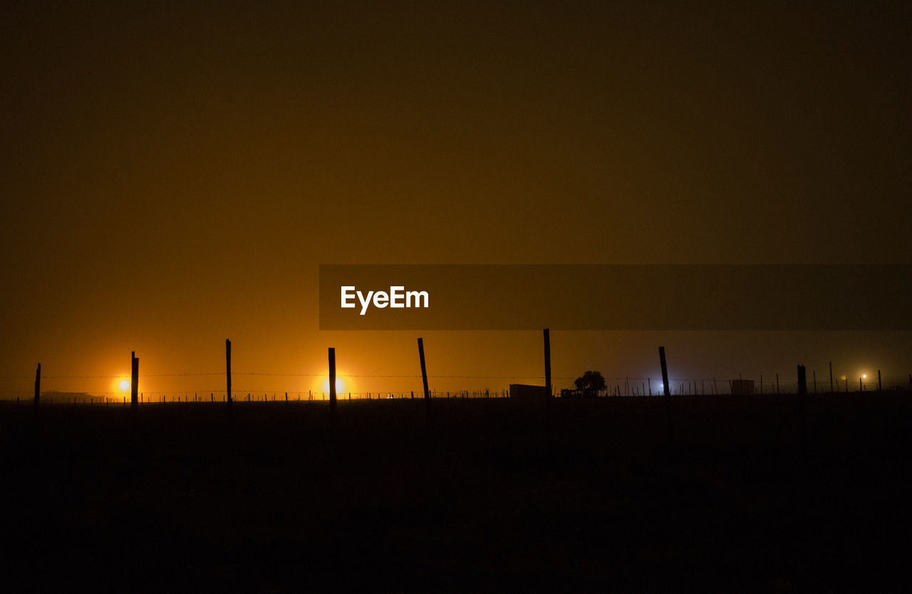 Silhouette fence against sky at night