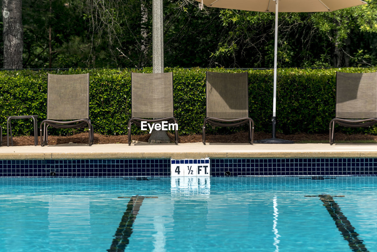 Swimming pool deck lounge chairs lined up by the side of a pool.