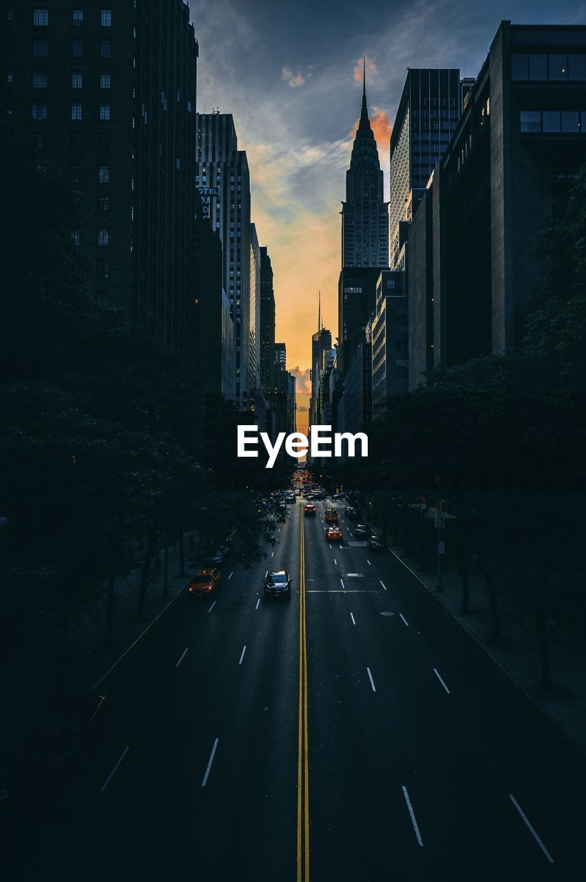 Road amidst buildings in city during sunset