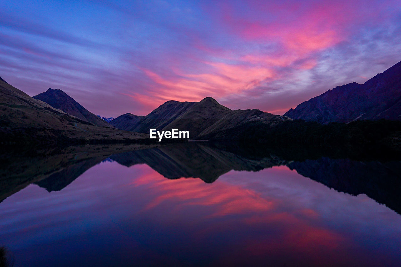 Scenic view of lake by mountains against sky at sunset