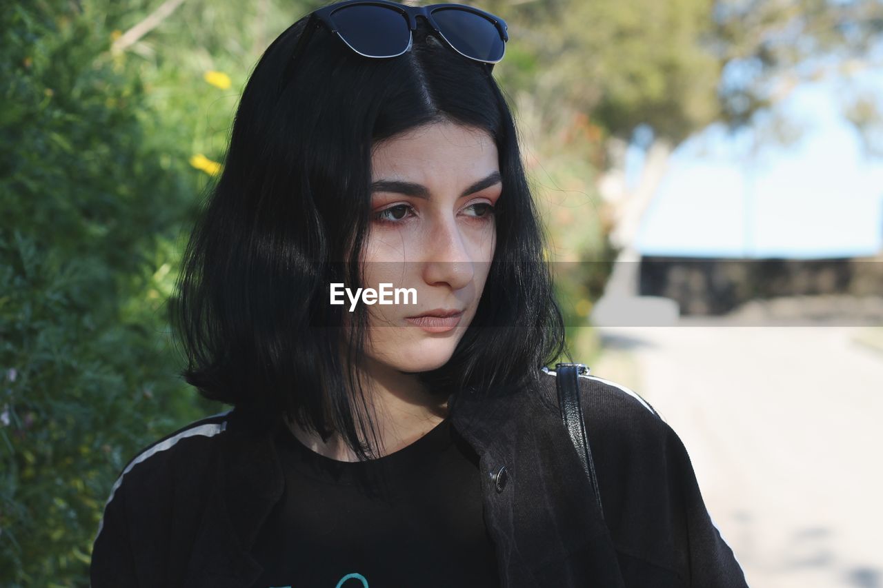 Close-up of thoughtful young woman standing against trees