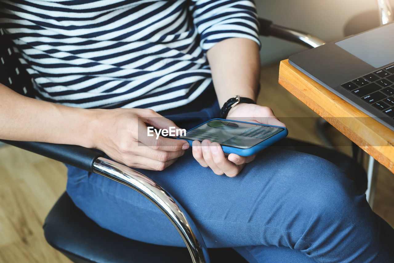 MIDSECTION OF MAN USING MOBILE PHONE WHILE SITTING AT HOME