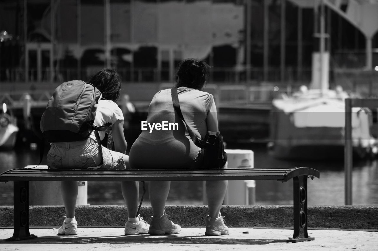 Rear view of people sitting on bench in city