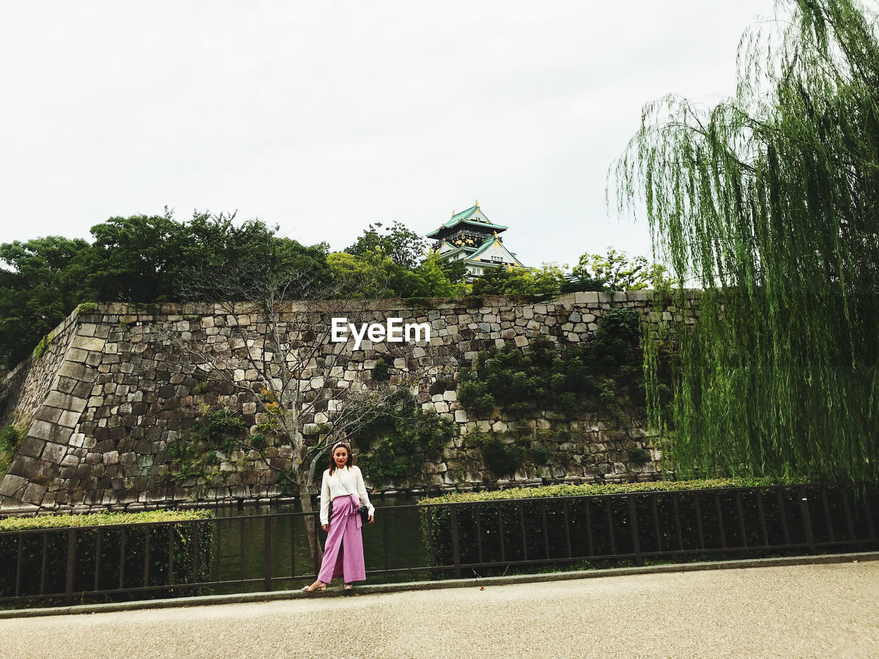 WOMAN STANDING BY TREES AGAINST BUILDING