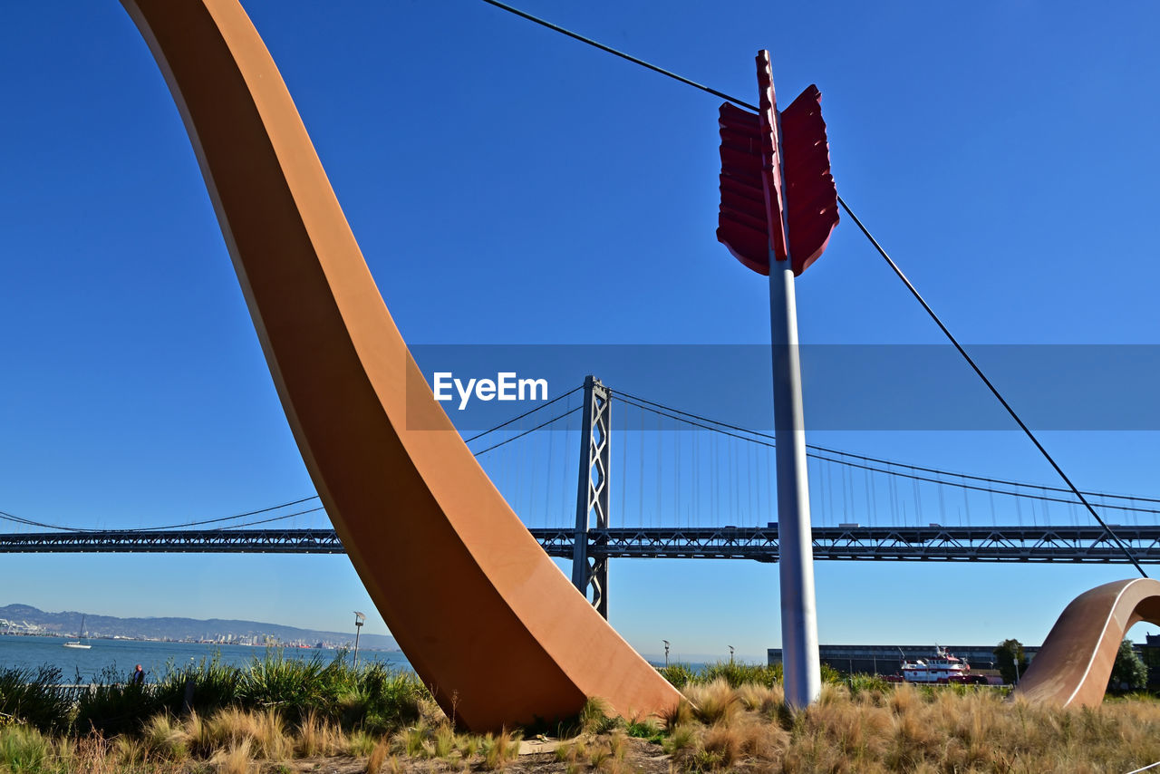 bridge, architecture, built structure, sky, nature, transportation, suspension bridge, travel destinations, cable-stayed bridge, blue, no people, travel, landscape, water, clear sky, tourism, day, environment, red, outdoors, city, scenics - nature, cable, land, sunny, plant, beauty in nature, tranquility