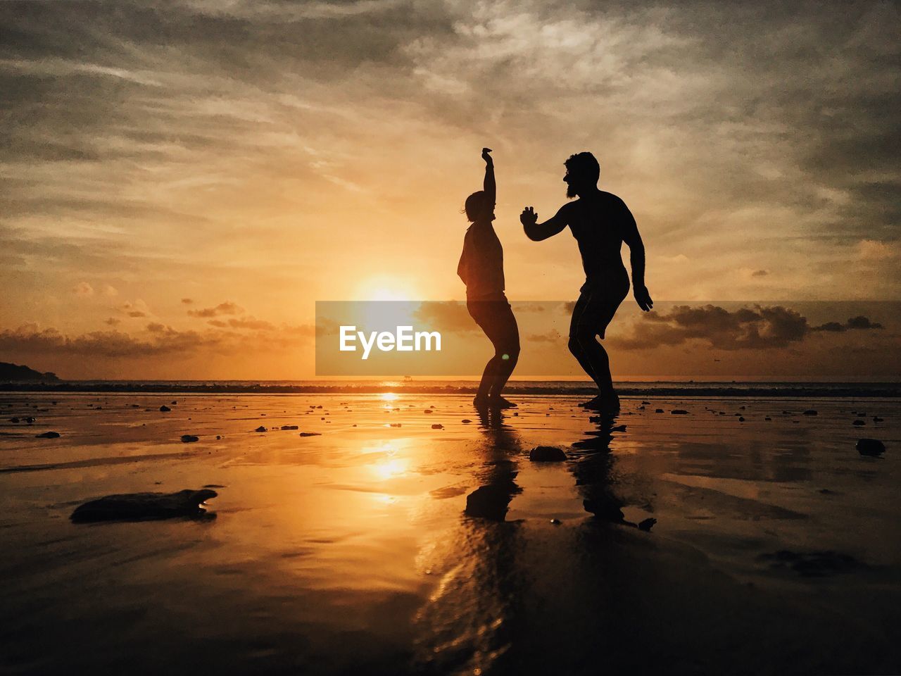 Silhouette friends dancing at beach against sky during sunset