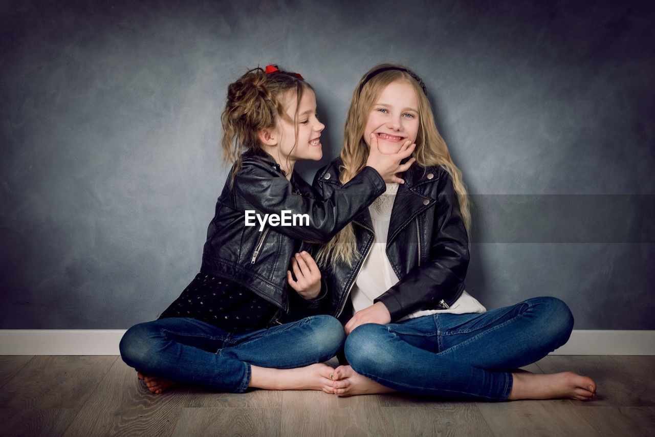 Portrait of cute girls sitting against wall