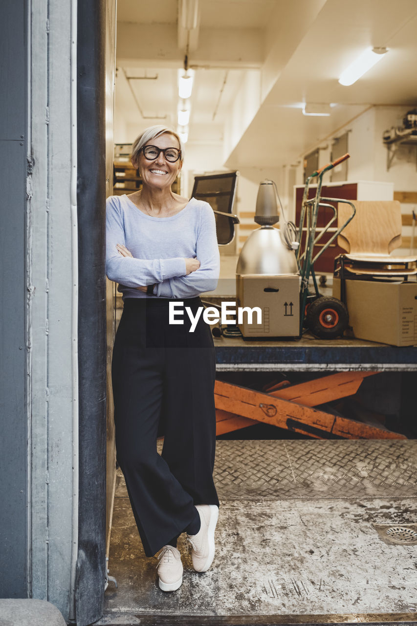 Full length portrait of smiling mature businesswoman standing arms crossed in new office