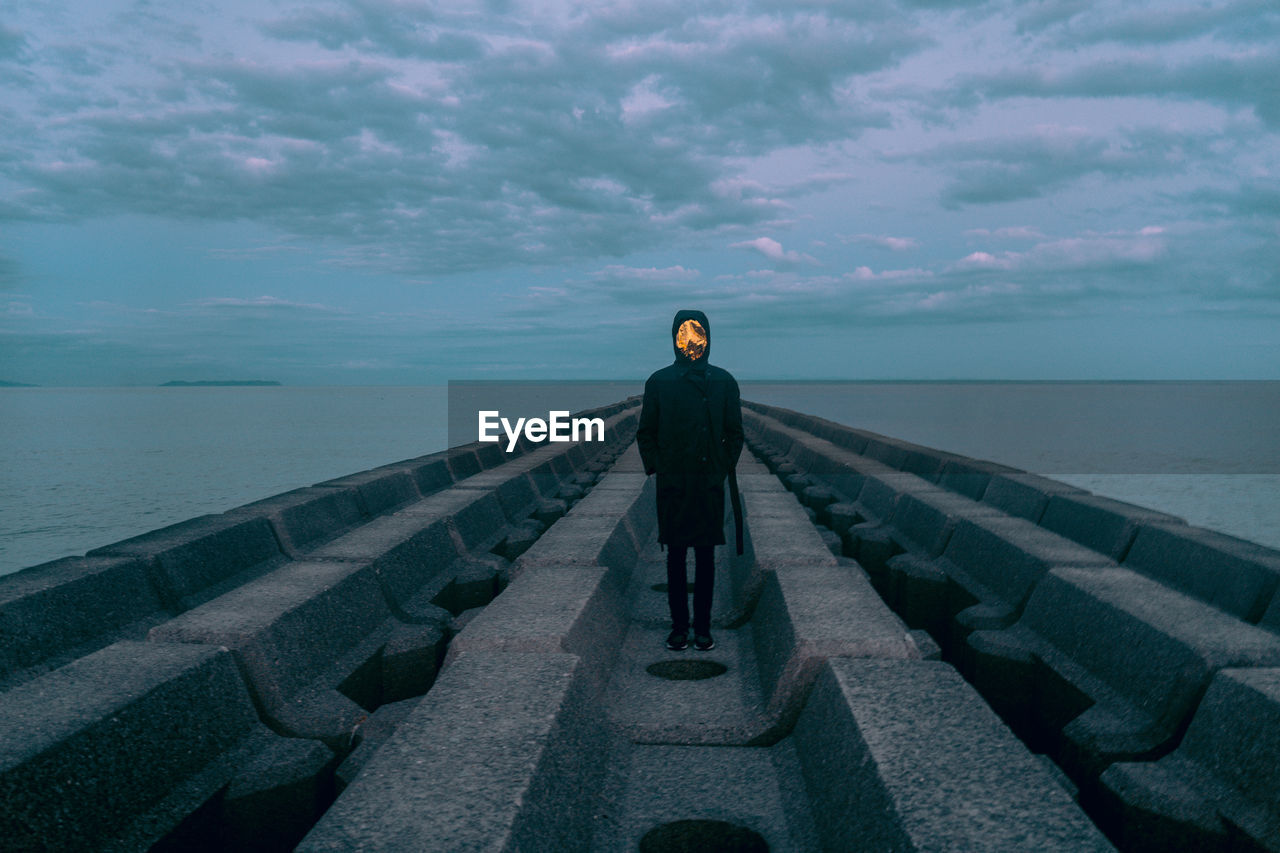 Rear view of man standing on rocks against sea and sky