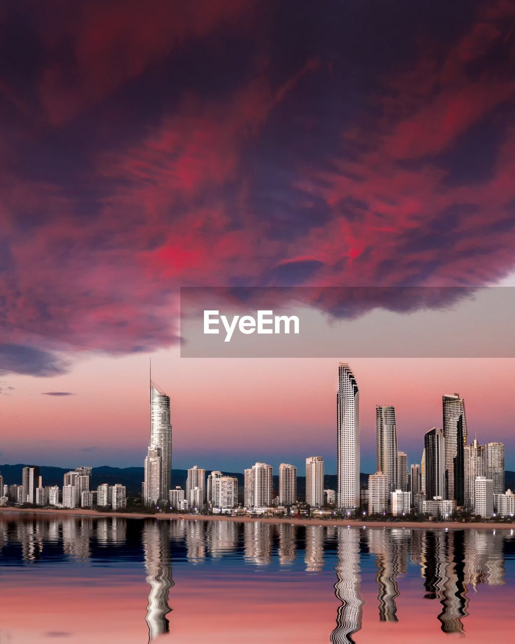 Reflection of buildings in sea against sky during sunset