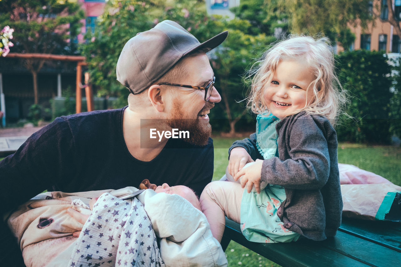 Happy father looking at daughter while holding son in park