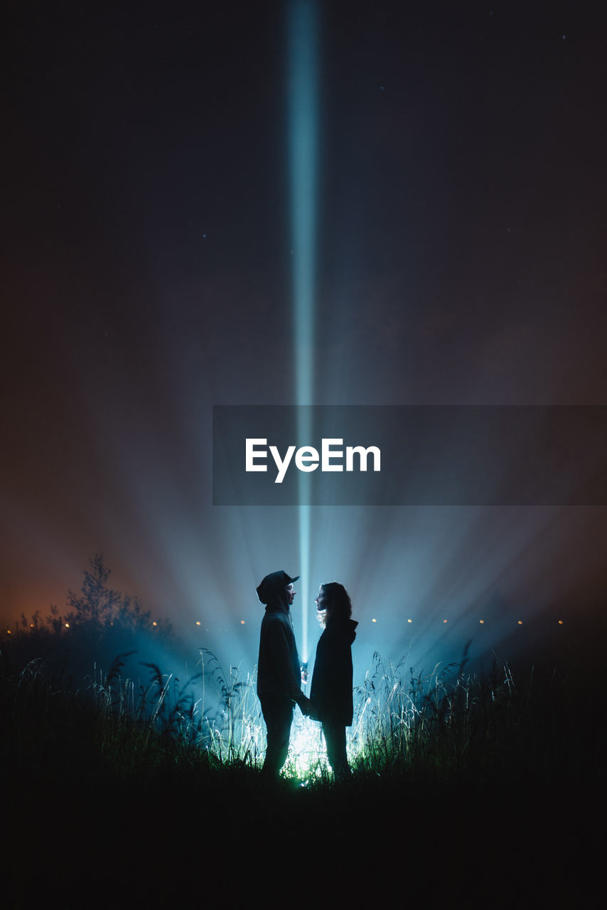 Couple standing on field against sky at night