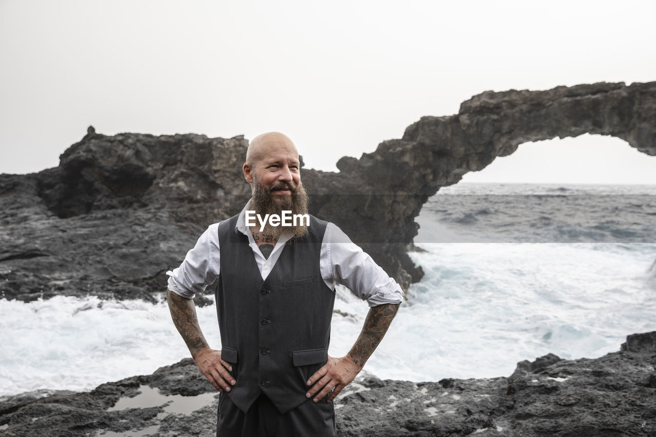 Mature man with hands on hip standing in front of sea