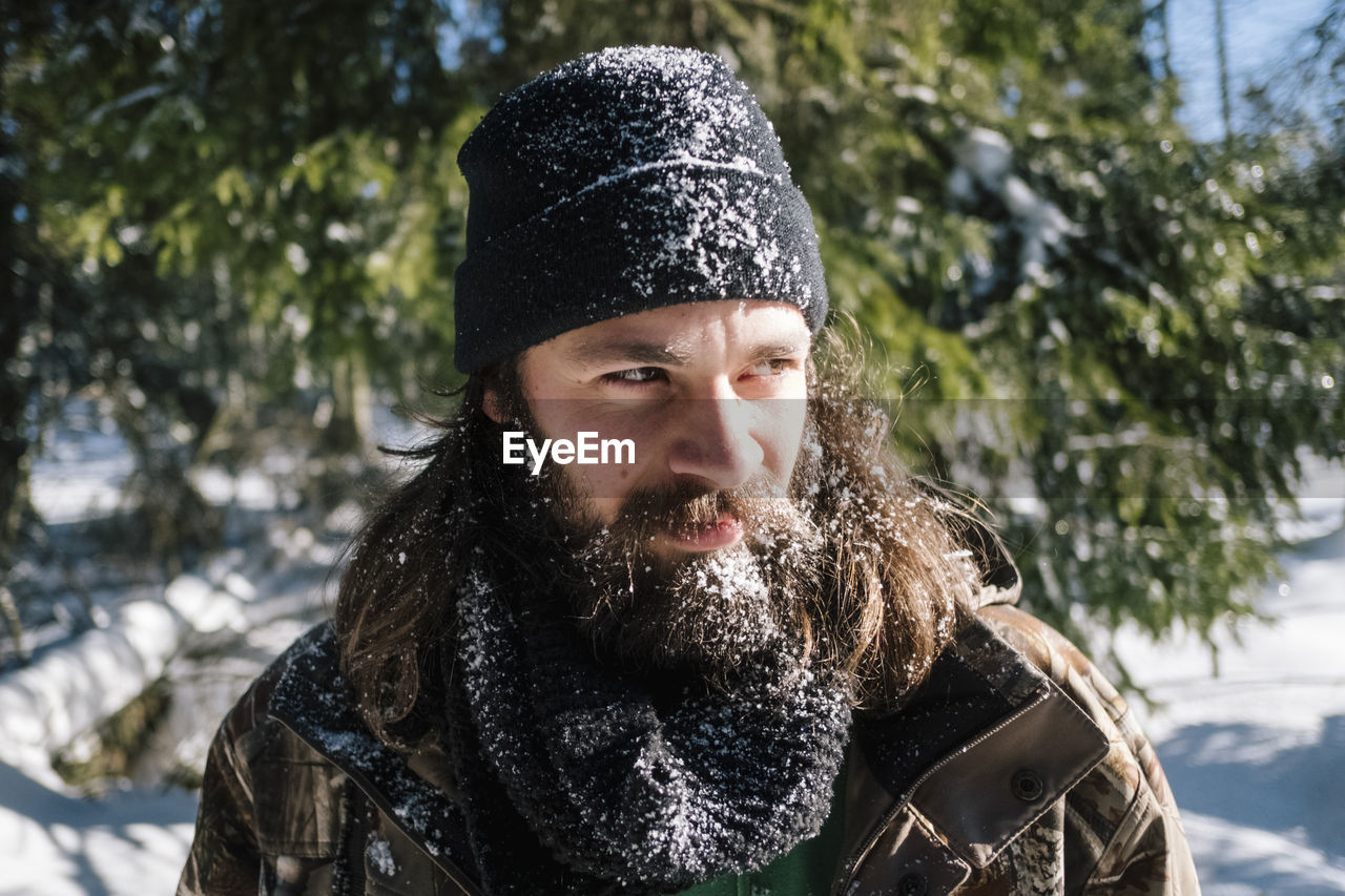 Bearded young man wearing warm clothing while looking away during winter