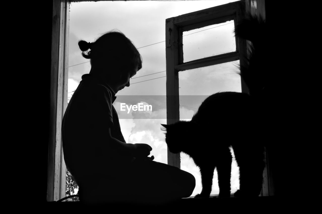 Silhouette girl with cat by window at home