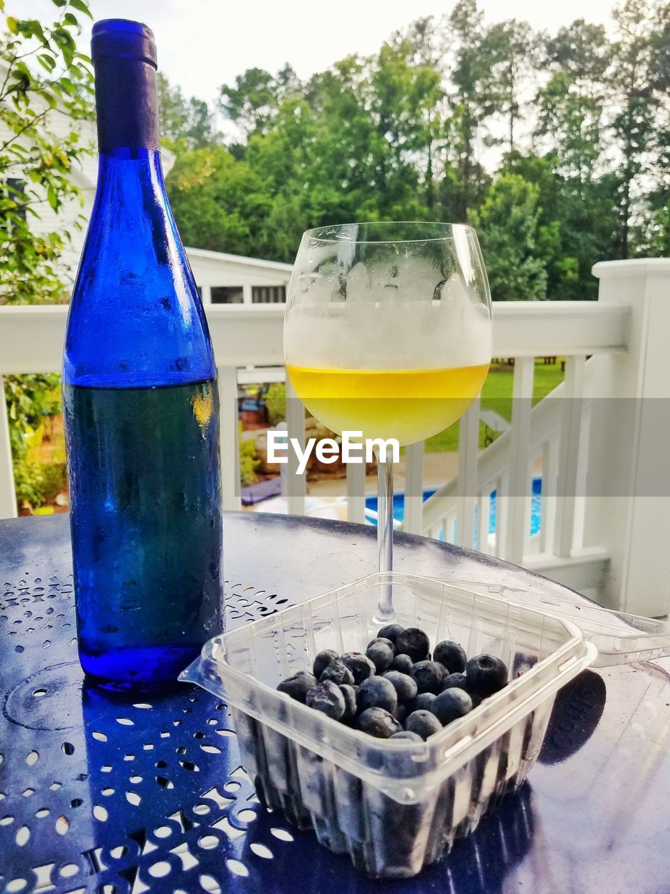 Bottle by wineglass and blueberries in container on table