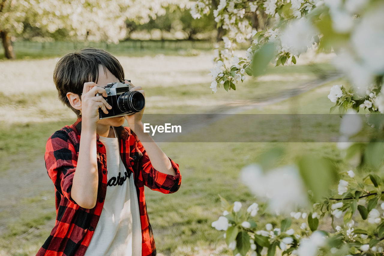 Boy photographing flowering plant outdoors