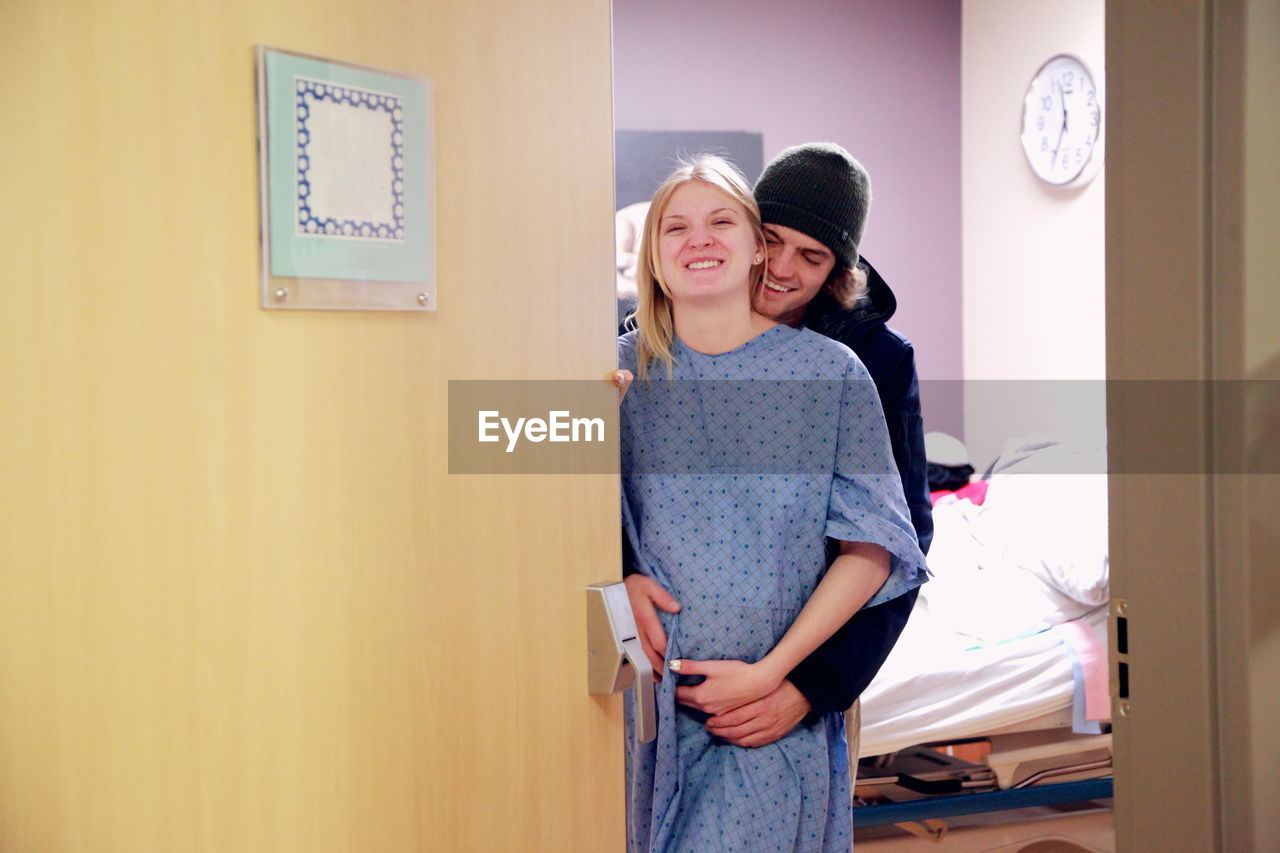 Portrait of a smiling young woman hugged by man in hospital