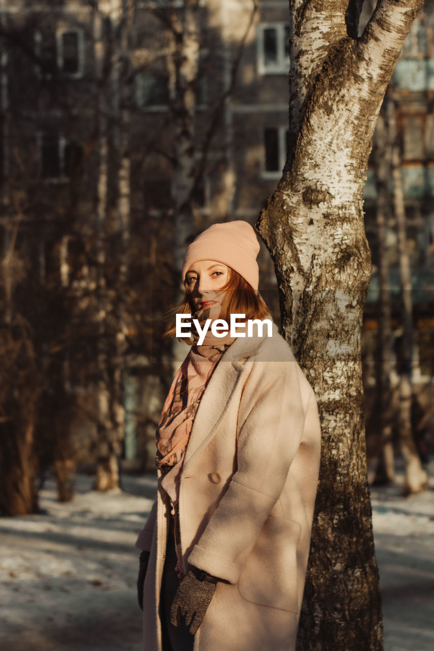 Portrait of woman standing by tree trunk during winter