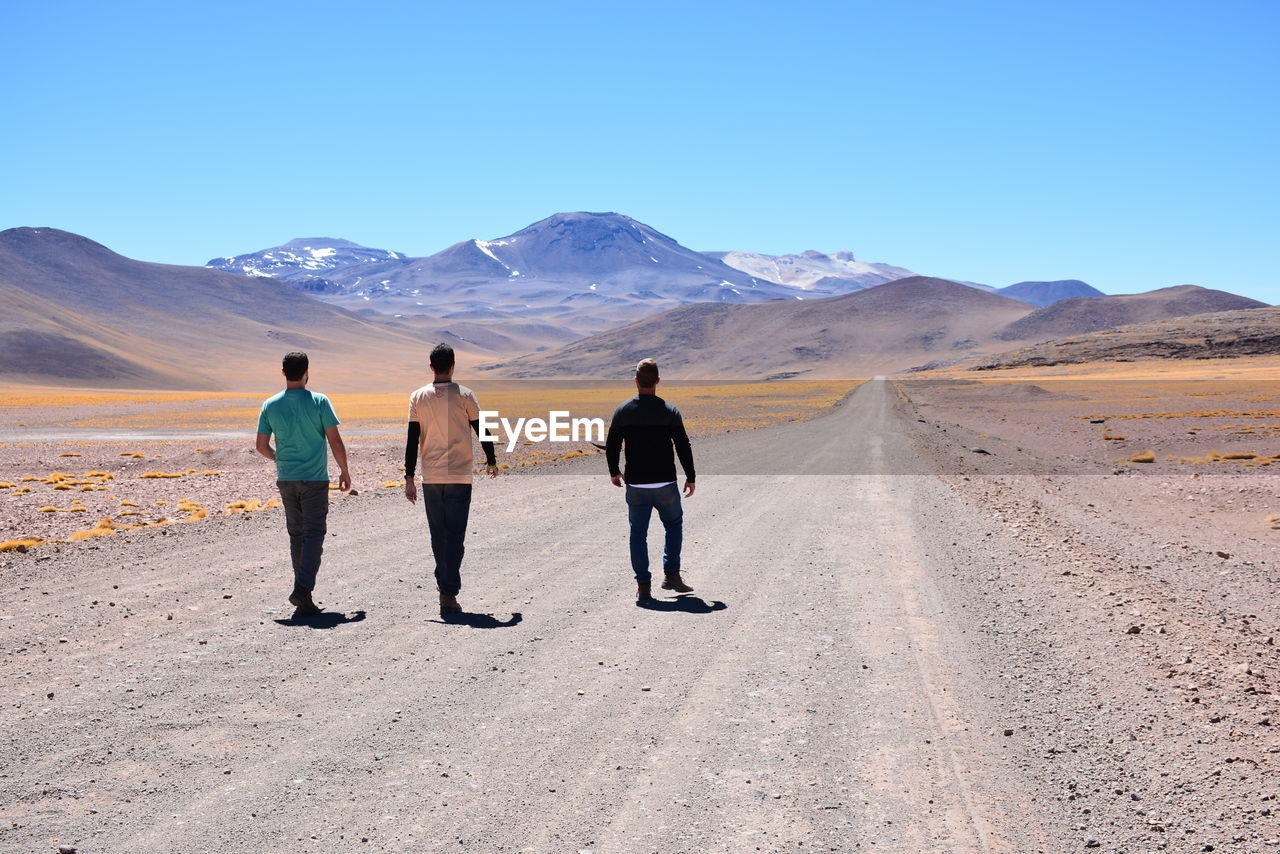 REAR VIEW OF MEN WALKING ON DESERT