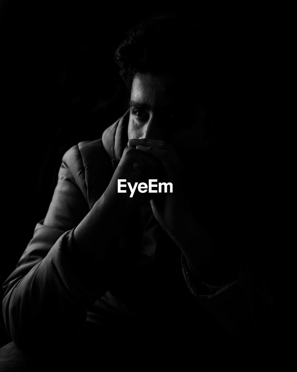 Young man sitting with hands clasped against black background