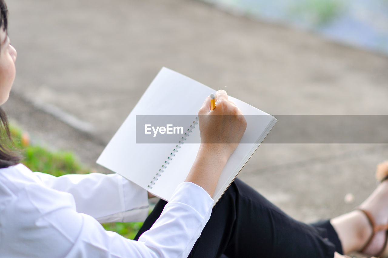 MIDSECTION OF MAN READING BOOK AGAINST WHITE BACKGROUND