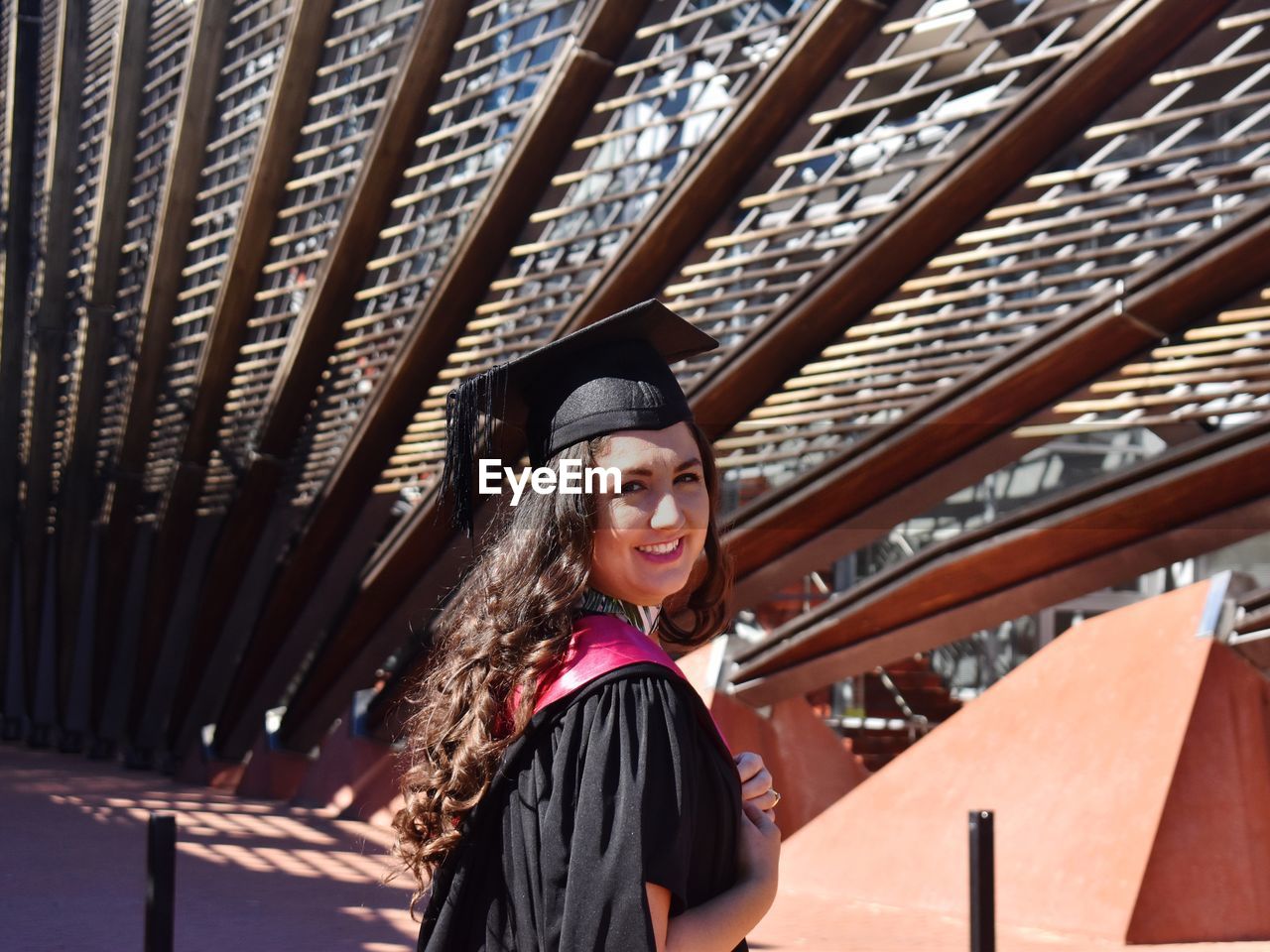 Portrait of smiling young woman standing against a building in graduation robes