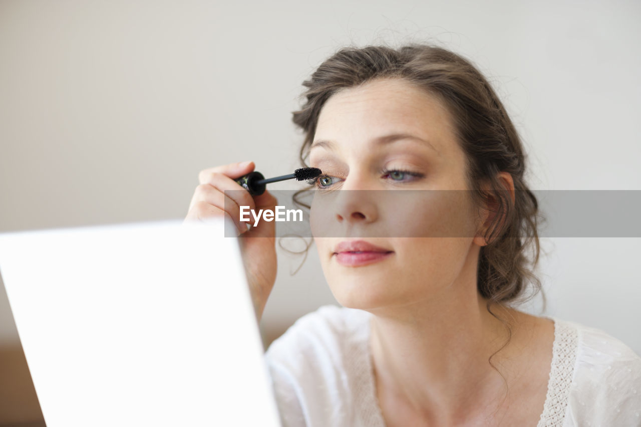 Woman looking in mirror applying mascara