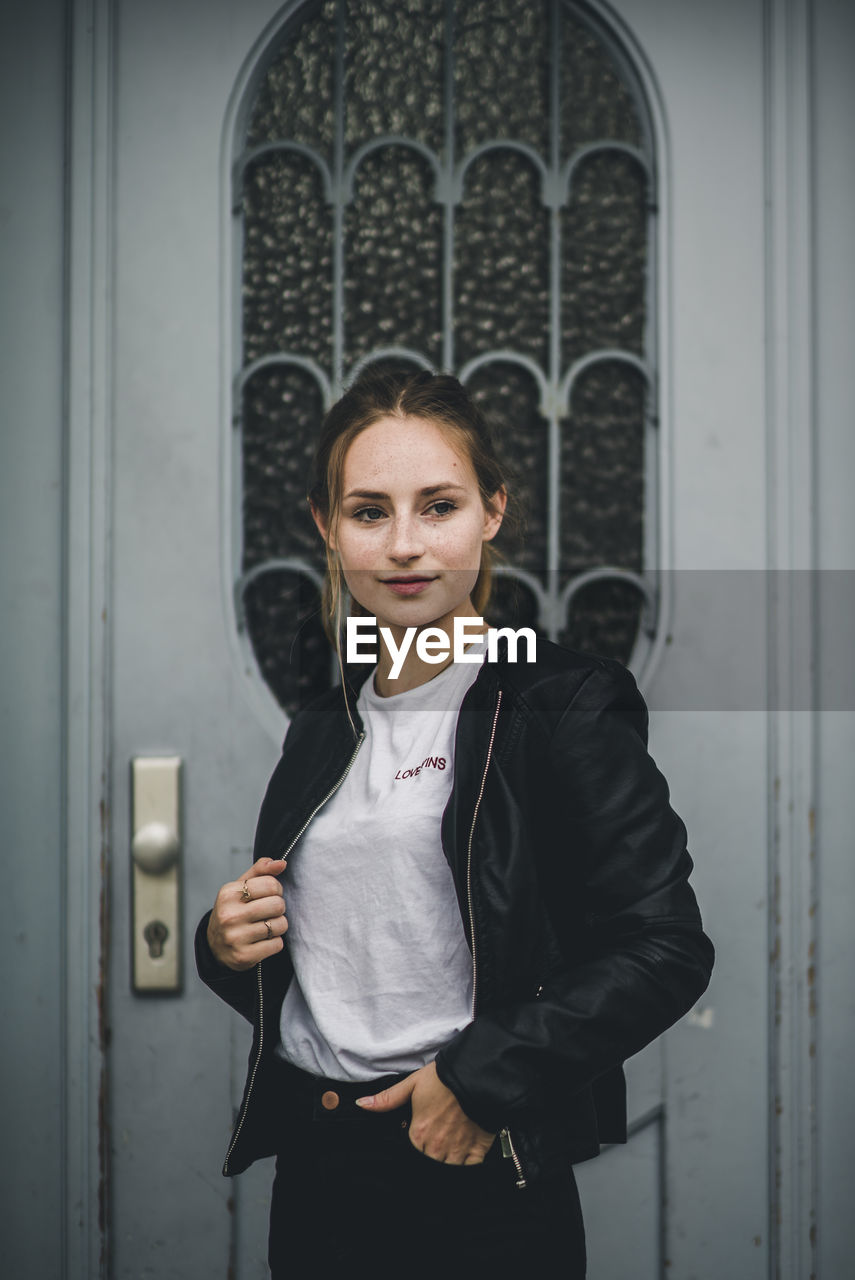 Young woman wearing leather jacket while standing by door